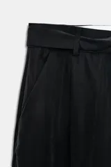 Pantalón negro de tiro medio con pierna ancha y pliegues frontales. Incluye un cinturón de lazo en el mismo tejido para ajustar a la cintura.