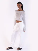 Sweater crop negro de punto abierto y manga larga con brillo sutil. Presenta escote bote y diseño relajado.