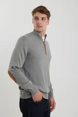 Sweater de punto gris con medio cierre frontal, cuello alto y coderas en tono marrón. Presenta un diseño clásico con puños y ruedo acanalados.