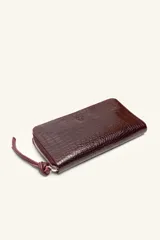 Billetera rectangular de cuero con textura de reptil, cierre perimetral y correa de muñeca lateral. Presenta un pequeño aplique metálico circular en el centro.
