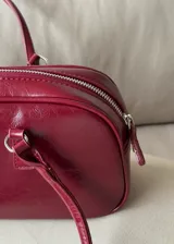 Cartera de mano tipo bowling color bordó, confeccionada en material sintético con textura arrugada. Cuenta con doble asa fija y cierre superior.