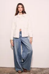 Sobrecamisa color blanco hueso de algodón, con cuello camisero, cierre frontal con botones a presión metálicos, bolsillos de parche en el pecho y bordados florales en los hombros. Corte holgado.