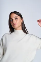 Sweater color beige de tejido de punto con cuello alto y mangas largas. Presenta detalles de ochos en diagonal en los laterales.