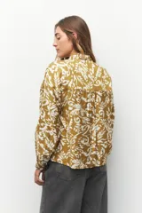 Camisa blanca con estampado floral en color marrón, de manga larga con puños abotonados, cuello con lazo y cierre frontal con botones.