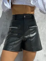 Short de tiro alto confeccionado en ecocuero elastizado, con bolsillos frontales amplios con cierre metálico.