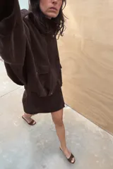 Falda mini de tiro medio confeccionada en tejido con efecto ante. Presenta un diseño cruzado con detalle de hebilla metálica en el lateral y cierre de cremallera oculta en la espalda.