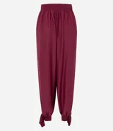 Pantalón de corte aladino con volumen en las piernas, confeccionado en tejido piquet. Presenta cintura elástica y detalle de lazos para anudar en los tobillos.