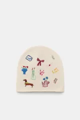 Gorro tipo beanie de punto color crema, con detalle de múltiples bordados coloridos que incluyen figuras como un perro salchicha, flores, lazos y objetos decorativos.