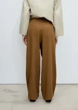 Pantalon de corte wide leg en color marrón, confeccionado en mezcla de algodón y lyocell. Presenta tiro medio, cierre frontal con cremallera y botón, trabillas para cinturón, bolsillos laterales y pinzas delanteras que aportan estructura.