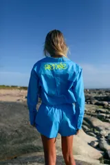 Camisa celeste de manga larga confeccionada en poplín de algodón. Tiene largo a la cintura y canesú estampado en plastisol.