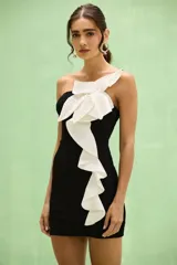 Vestido corto negro de un solo hombro, con gran aplicación floral blanca estructurada en el escote y volado vertical en cascada del mismo color al frente.