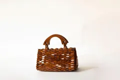 Cartera de mano marrón de diseño artesanal, elaborada con piezas de madera encadenadas en forma de escamas y asas rígidas de madera.