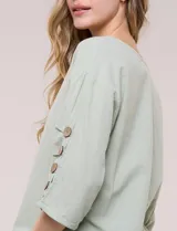 Blusa Erika de algodón con estampado de rayas en tonos azules, rosados y amarillos. Presenta cuello redondo con escote en V y botones frontales, mangas cortas decoradas con una fila de botones en los laterales y dobladillo asimétrico.