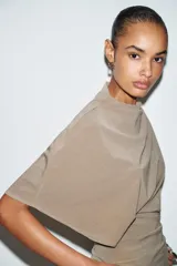 Top fluido color beige, con cuello perkins y mangas por debajo del codo. Bajo redondeado.