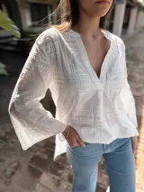 Blusa blanca de broderie con cuello mao y escote en V, mangas largas acampanadas y bordados calados.