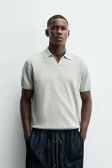 Jersey de punto color verde oliva, de calce relajado (relaxed fit), con cuello solapa y abertura frontal en forma de V. Es de manga corta y presenta acabados en rib en puños y ruedo.