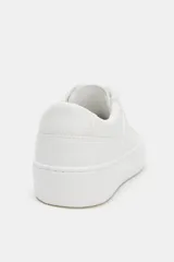 Zapatilla deportiva blanca de mujer, estilo casual con plataforma. Presenta cordones blancos y detalles de costuras y paneles texturizados en el lateral.