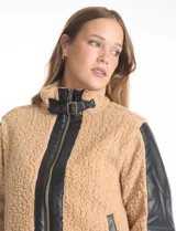 Campera de corderito sintético color beige con paneles y detalles en cuero sintético negro. Presenta cuello alto con tira y hebilla metálica, cierre frontal metálico y mangas largas con paneles de cuero sintético.