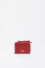 Monedero o tarjetero pequeño de cuero rojo, con cierre de cremallera superior y un tirador de tela a juego. Presenta un bolsillo exterior frontal y el logo de la marca grabado en dorado.