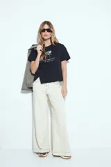 Remera blanca de manga corta con estampa frontal de un personaje con lentes de sol y la frase "Llegué tarde porque no quería venir". Tiene silueta relajada y calce cómodo, con un corte asimétrico en el bajo.