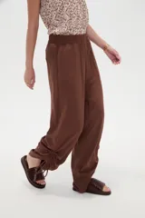 Pantalón verde militar de corte ancho y tiro alto, con cintura elástica fruncida y detalles de cordones ajustables en los tobillos.