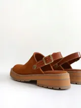 Zueco de cuero gamuzado color óxido, con tira trasera ajustable mediante hebilla metálica. Presenta una suela de plataforma con textura acanalada y detalle de textura reptil en la tira posterior.