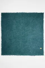 Chal cuadrado de cachemir color verde azulado con flecos en los bordes y etiqueta con el logo de la marca en una esquina.