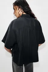 Camisa de manga corta color marrón oscuro, con cuello solapa, cierre frontal oculto con botones y dos bolsillos de parche en el pecho.