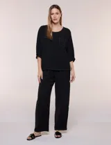 Blusa oversize color negro con caída fluida, escote redondo, bolsillo frontal en el pecho, mangas tres cuartos de hombro caído y costuras a la vista en contraste.