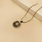 Collar con dije circular de San Benito, elaborado en una combinación de plata y oro. El dije presenta un diseño detallado con acabado envejecido y una pieza central dorada. La cadena es de tipo soga con eslabones metálicos.