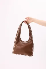 Cartera estilo hobo color marrón de cuero sintético con tachas metálicas plateadas en los bordes.