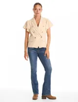 Chaqueta sastrera Nanette color beige, con cuello de solapa, escote en V y cierre cruzado con doble abotonadura. Presenta mangas cortas con volados, bolsillos delanteros simulados y ruedo frontal con acabado en pico.