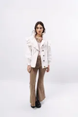 Campera de pana color blanco, de corte oversize, con cuello alto, cierre frontal de botones y volados decorativos en los hombros y cuello.