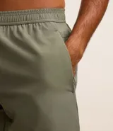Bermuda deportiva masculina color verde oliva, confeccionada en poliéster y elastano. Posee cintura elástica con cordón interno ajustable y estampa reflectante en el lateral. Ideal para actividades deportivas.