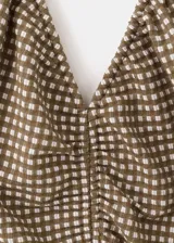 Vestido midi de corte evasé con estampado de cuadros vichy en tonos marrón y blanco. Presenta escote halter con tirantes finos para anudar al cuello, detalle fruncido en el centro del pecho y falda amplia de largo midi.