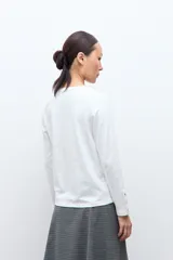 Remera de manga larga en color blanco, con cuello redondo y detalle de botones en los puños.