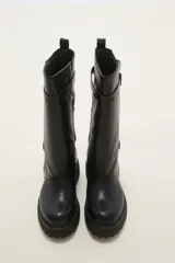 Bota de caña media en color negro, confeccionada en eco cuero con suela track dentada. Presenta un diseño con doble tira ajustable con hebillas metálicas en el lateral externo.