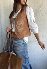 Chaleco de gamuza color camel con bordados decorativos en color blanco y cierre frontal con cordones y apliques metálicos.