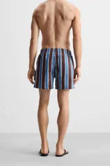 Short de baño confeccionado en tejido técnico con diseño de rayas verticales en tonos azul, marrón y beige. Cuenta con cintura elástica ajustable con cordón, bolsillos laterales y forro interior.