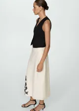 Falda midi de tiro alto con corte evasé, confeccionada en una mezcla de algodón y lino color beige. Presenta un diseño bordado floral en color negro ubicado en el lateral inferior.