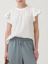 Blusa de manga corta color blanco, con cuello redondo y detalles de crochet en las mangas. Presenta un cierre de botón en la parte posterior del cuello.