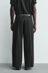 Pantalón chino de corte wide fit confeccionado en tejido de algodón. Presenta pliegues frontales, bolsillos laterales y bolsillos traseros de vivo, con cierre frontal de cremallera y botón.