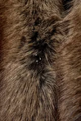 Chaqueta bomber negra de corte corto y diseño abullonado, con cuello de solapa amplio en pelo sintético marrón. Cuenta con mangas largas y cierre frontal.