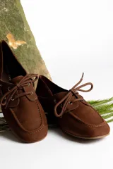 Mocasín de cuero marrón con cordones, diseño de puntera cuadrada y costuras visibles.
