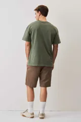 Remera de calce relajado y cuello redondo, color verde musgo con efecto lavado, y pequeño bordado de un morrón en el pecho.