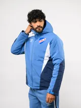 Campera de abrigo Umbro del Club Nacional de Football, con diseño de bloques de color en azul, blanco y rojo. Cuenta con capucha ajustable, cierre frontal y logo de la marca junto al escudo del club en el pecho.
