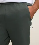 Pantalón deportivo de corte ajustado, confeccionado en tejido de poliéster texturizado color negro. Presenta cintura elástica con cordón de ajuste, bolsillos laterales con cierre y puños elásticos en los tobillos.