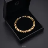 Pulsera de eslabones gruesos con baño de oro, destacada por un cierre central de diseño ornamental en forma de flor de lis con acabado plateado.