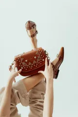 Cartera bandolera de cuero 100% natural color marrón, con estructura armada y tapa decorada con tachas plateadas colocadas a mano. Forrada en tela con bolsillo interno con cierre.