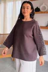 Sweater gris melange con detalles de perlas y strass aplicados en las mangas, de corte holgado y mangas largas.